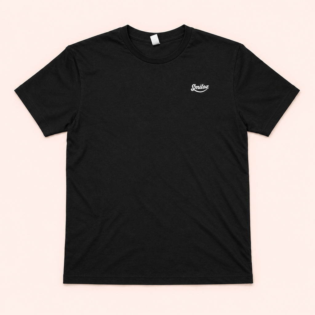 Front of black Smiloz T-shirt with small white chest logo on a blush background