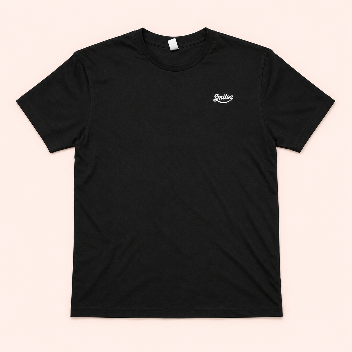Front of black Smiloz T-shirt with small white chest logo on a blush background