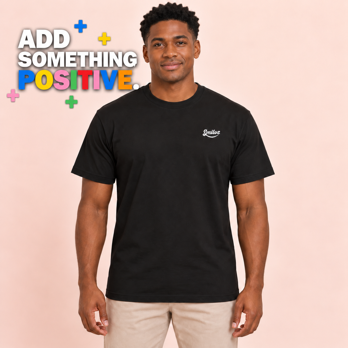 Front view of model wearing the black Smiloz Multicolour Plus signs T-shirt with Add Something Positive campaign slogan